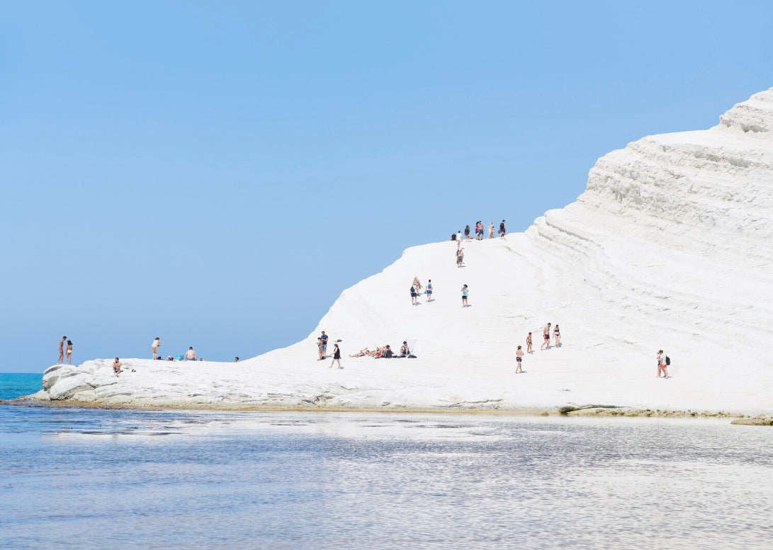photograph of people standing on a snowy mountain next to the water