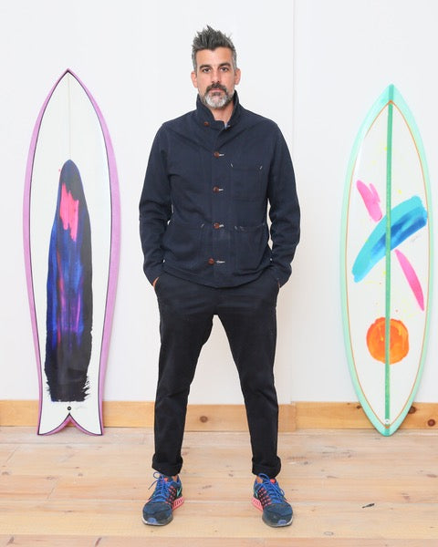 photo of Justin Cox standing next to two colorful surfboards with abstract design