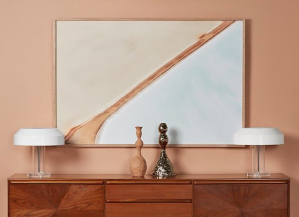 abstract painting hung above entrance wooden table with two sculptures and lamps