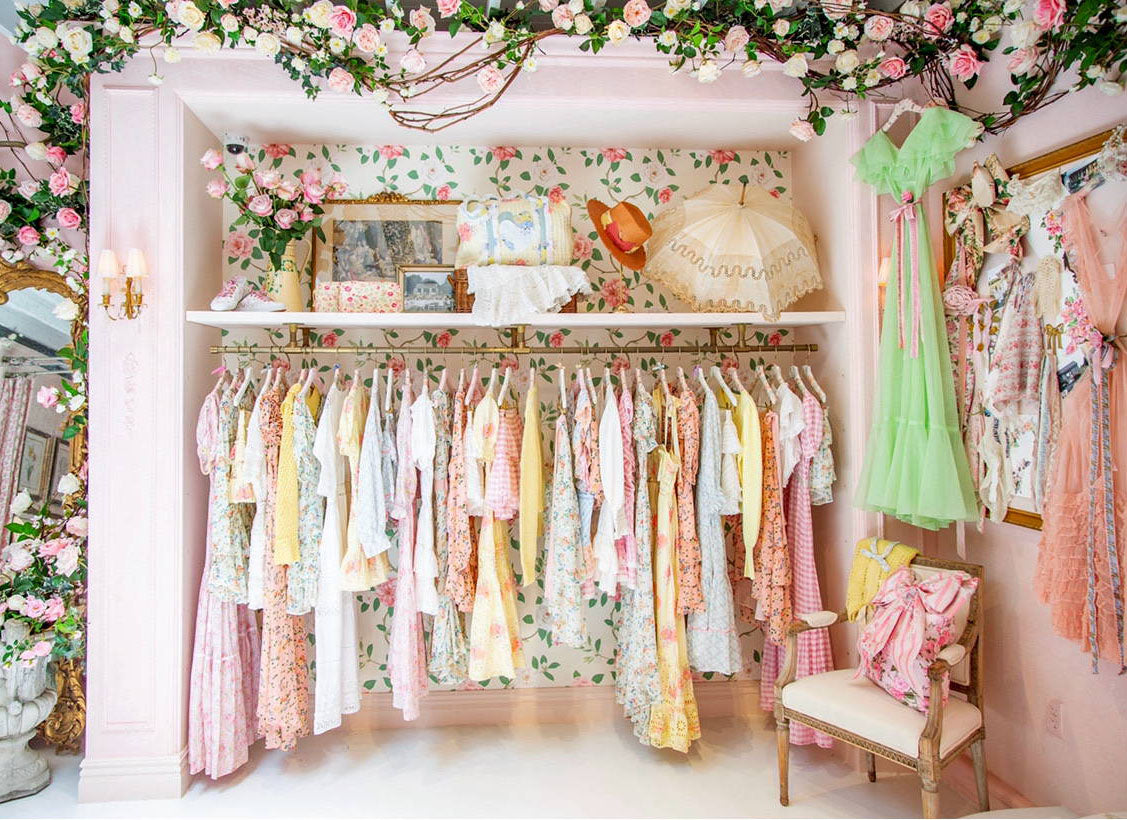 Love Shack Fancy pastel colorful dresses on rack in store surrounded by flower garland