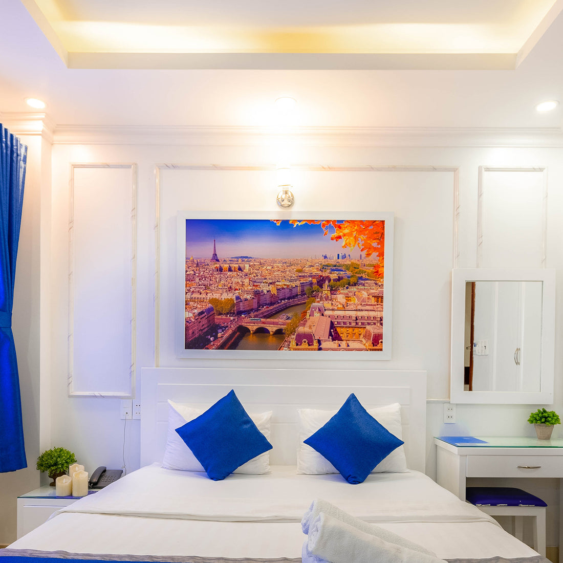 custom framed aerial view of Paris in the fall hung in a white frame in a hotel room over a bed with white sheets and royal blue pillows