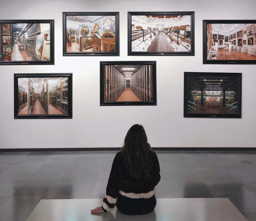 woman sitting on a bench in an art gallery looking at photographers photos that are hung and framed in skyframe black frames