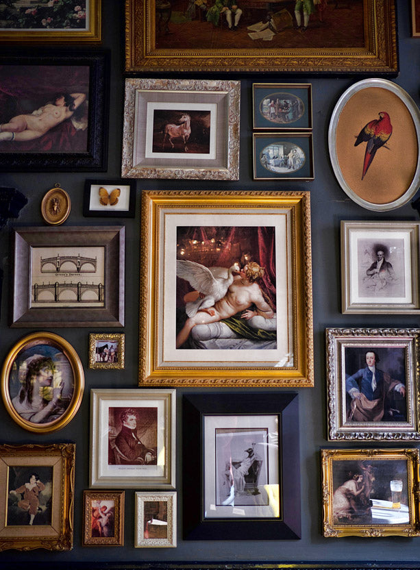 gallery wall covered in many framed paintings. all the frames are different sizes, shapes and colors 