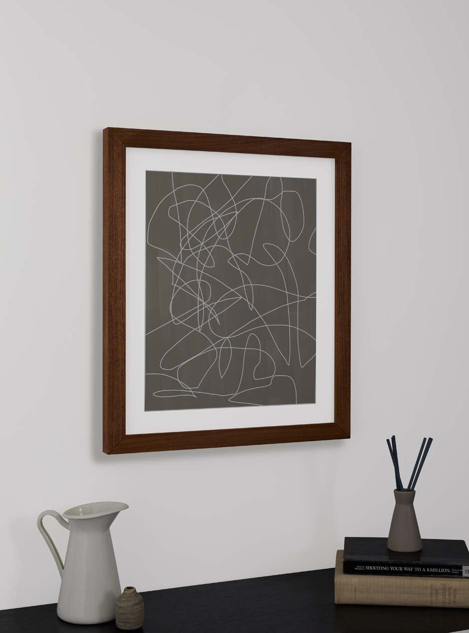 brown wooden frame holding abstract art hung above table with various objects 