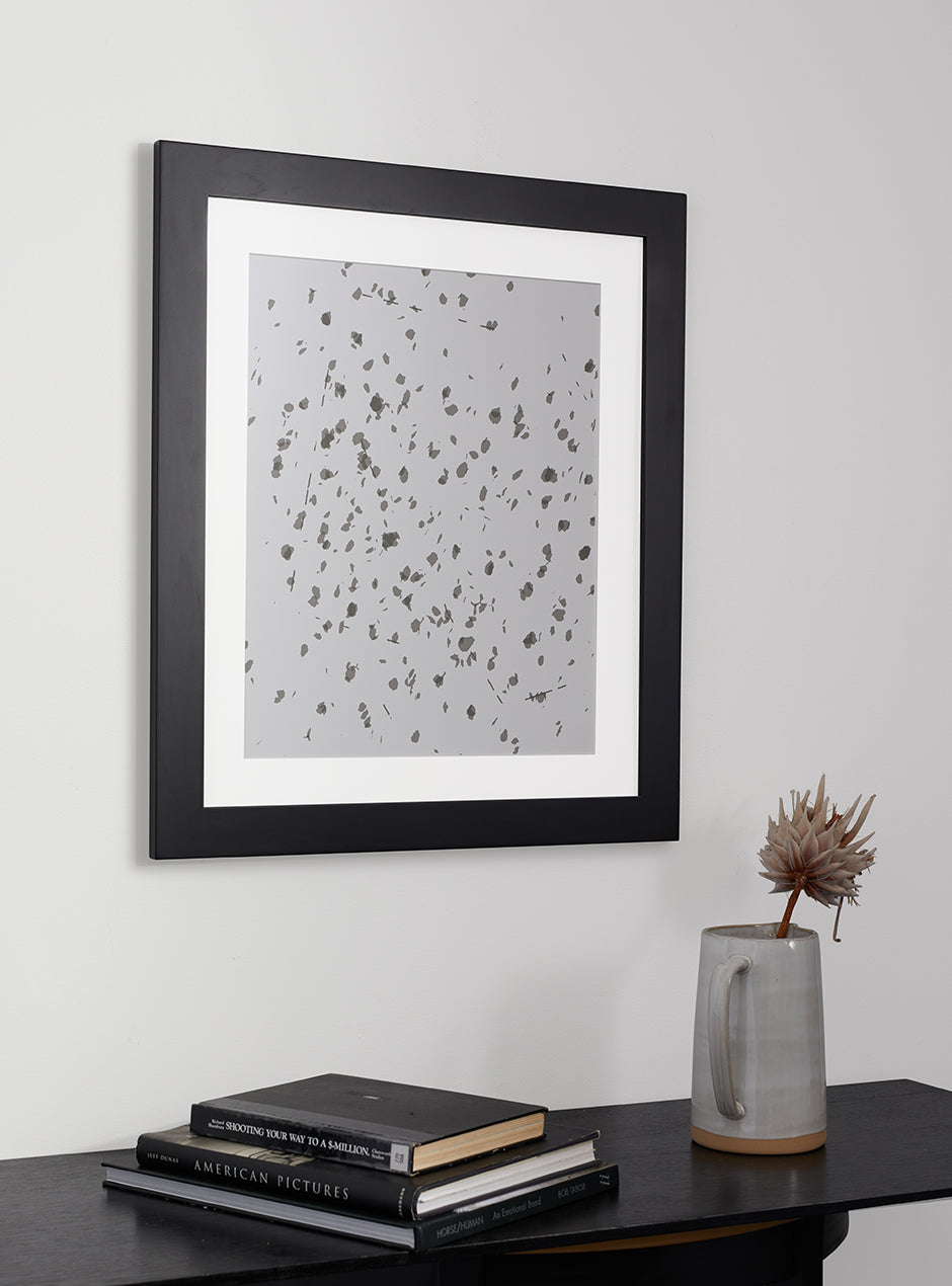 Black frame holding abstract art hung above table with various objects 