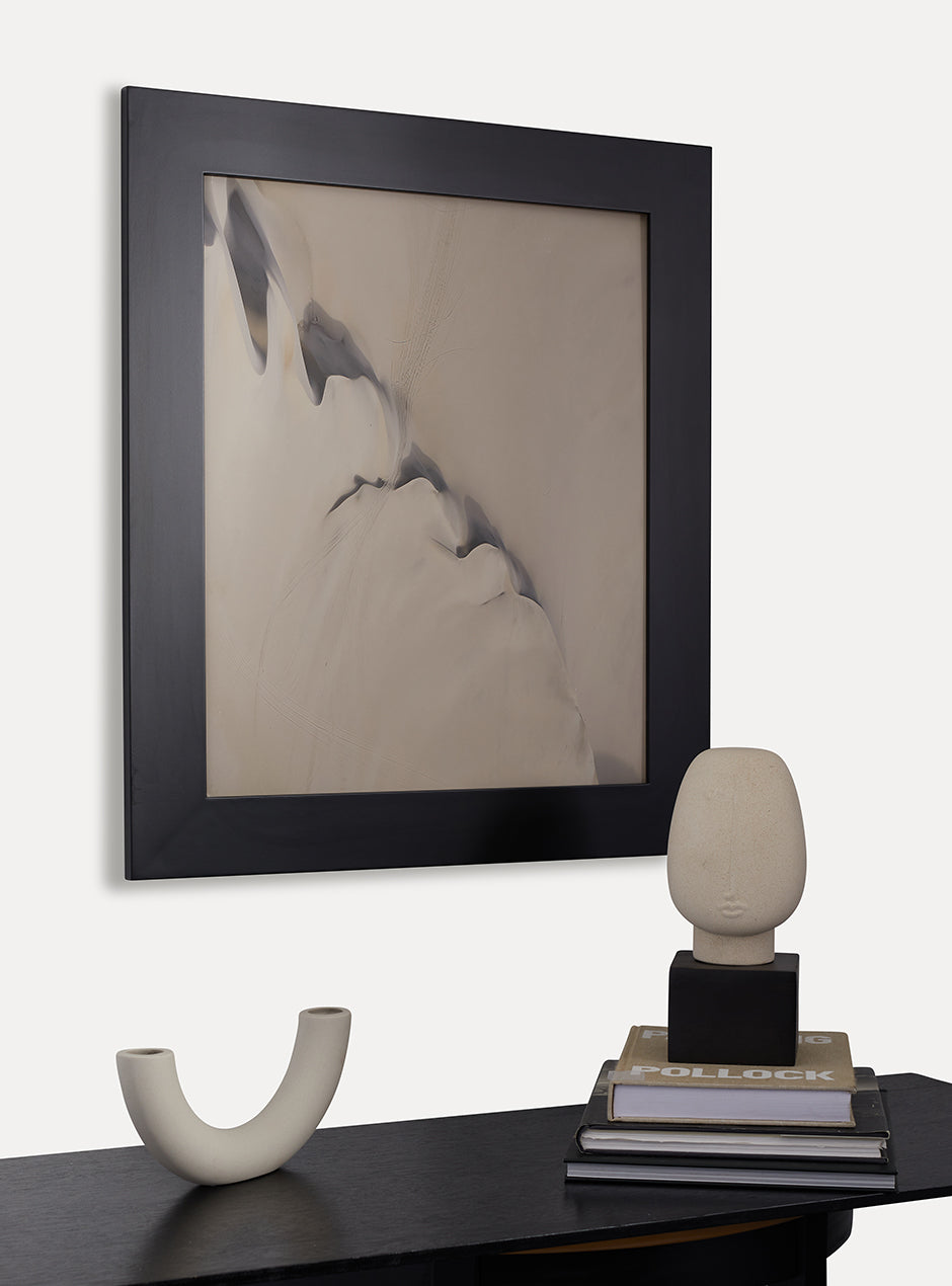 Black frame holding abstract art hung above table with various objects 