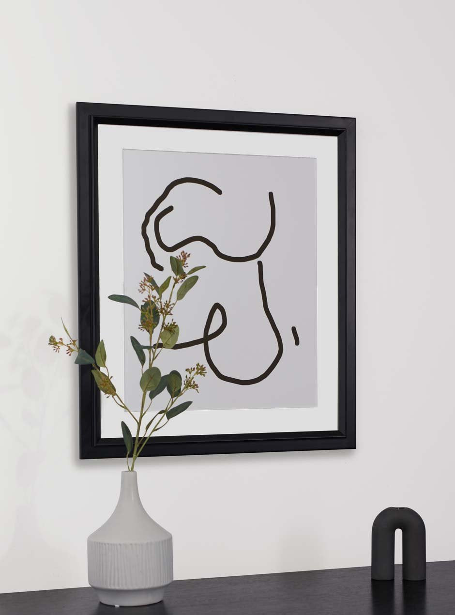 black matte frame holding abstract art hung above table with various objects