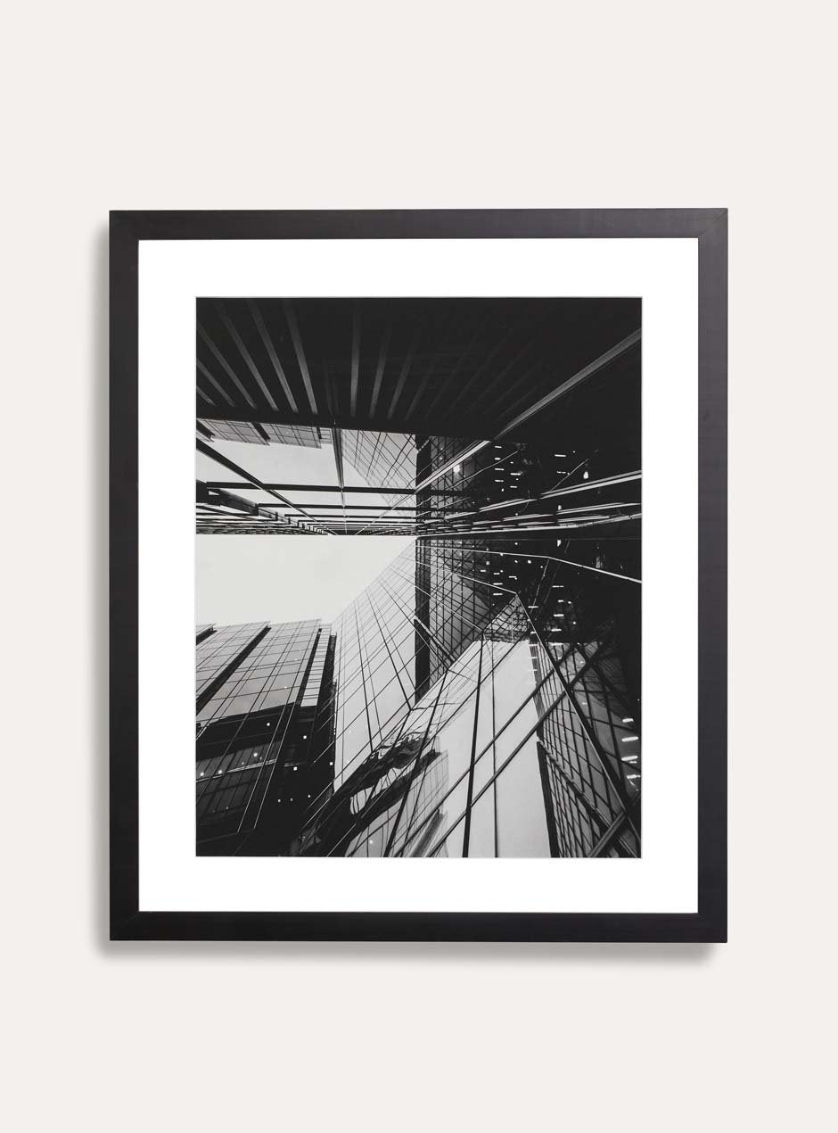 modern black frame called the alma that is 1/2 inch wide facing the front with a white mat and a black and white photograph of a reflective new york city building