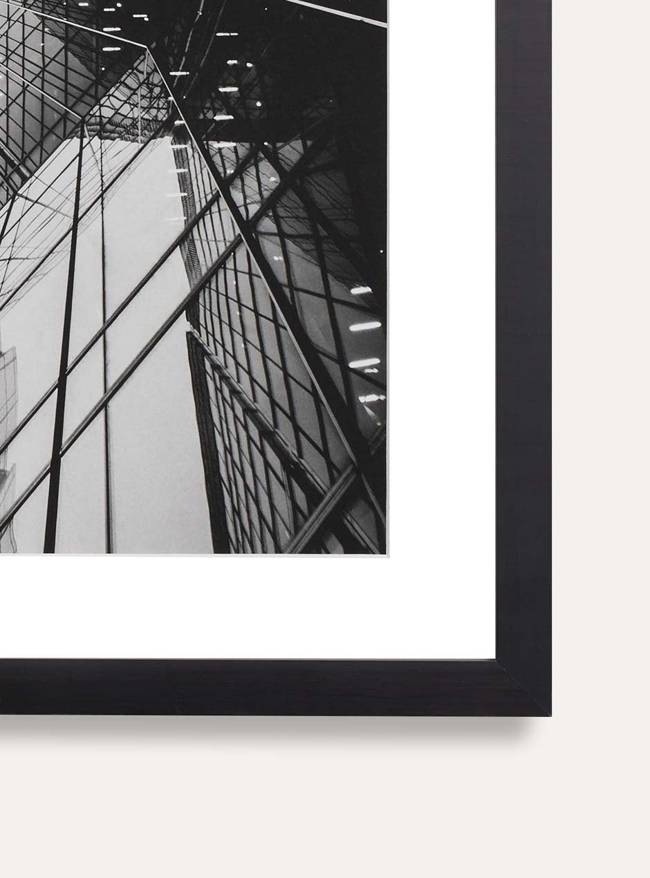 detail photo showing texture modern black frame called the alma that is 1/2 inch wide facing the front with a white mat and a black and white photograph of a reflective new york city building