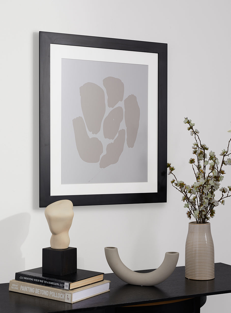 black frame with abstract art hung above table with various objects 
