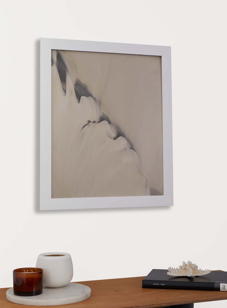 white frame holding abstract art hung above table with various objects 