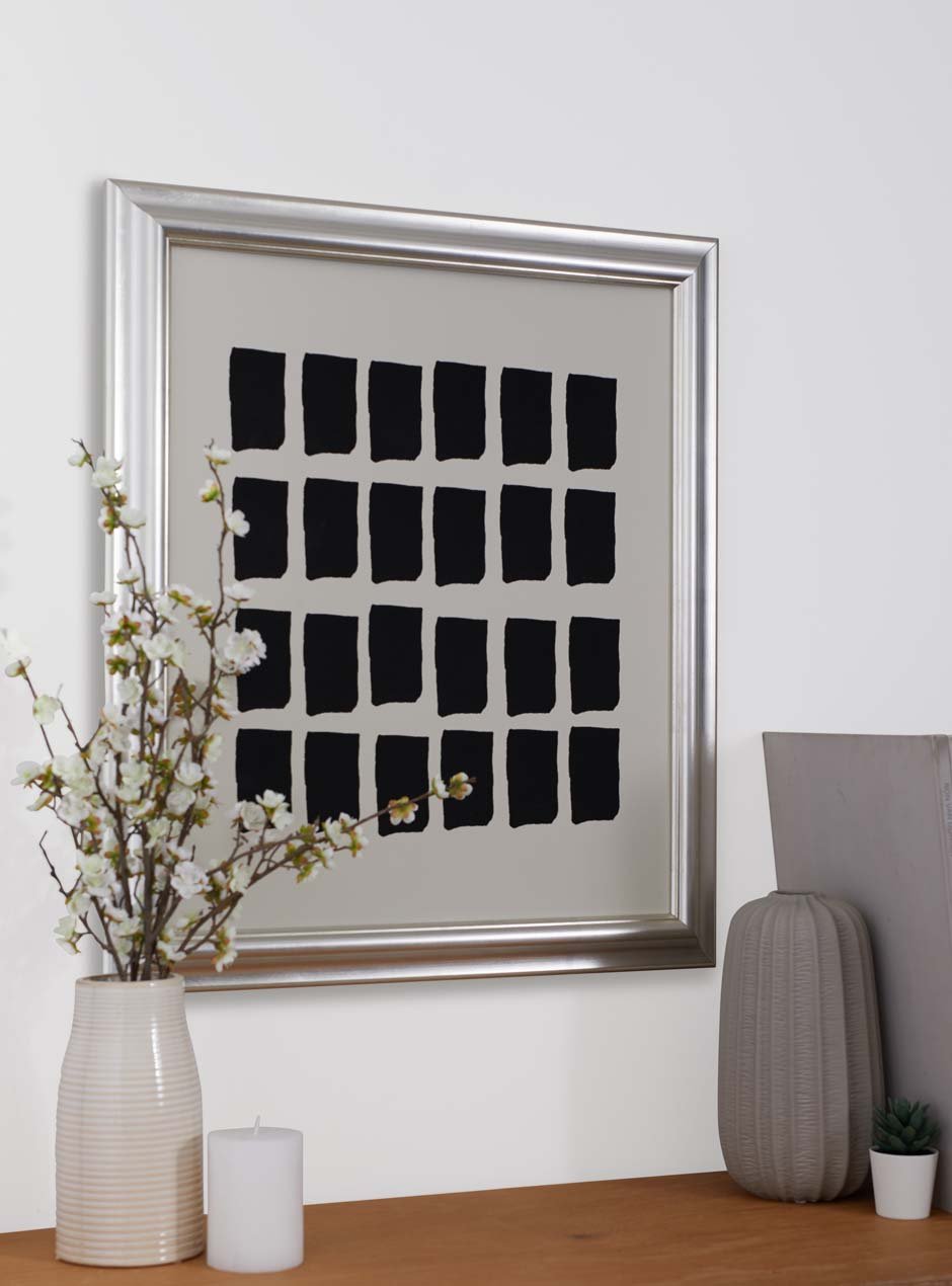 high quality metallic silver moulding shiny picture frame detailed with several grooves showing modern black paint pieces above a solid wooden table with a vase that contains white flowers and another empty light grey modern vase