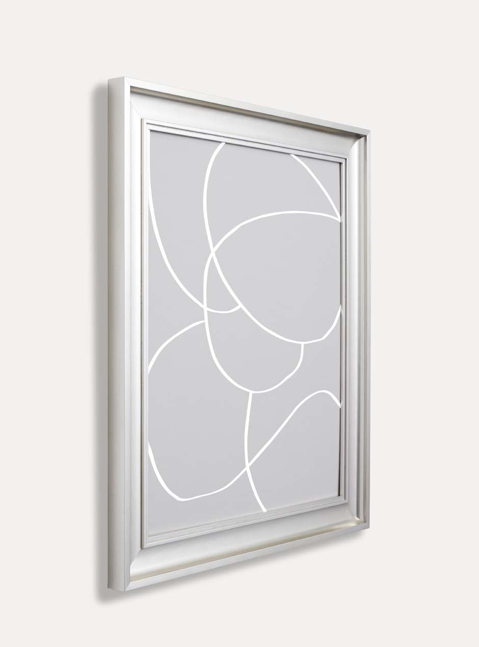 side profile silver metallic shiny picture frame with depth and higher ridges showing circular modern abstract grey art against white wall