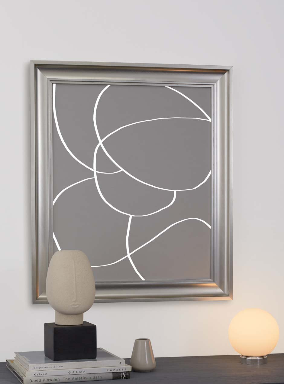 silver metallic shiny picture frame with depth and higher ridges showing circular modern abstract grey art against white wall with modern face statue and lit spherical lamp below modern apartment 
