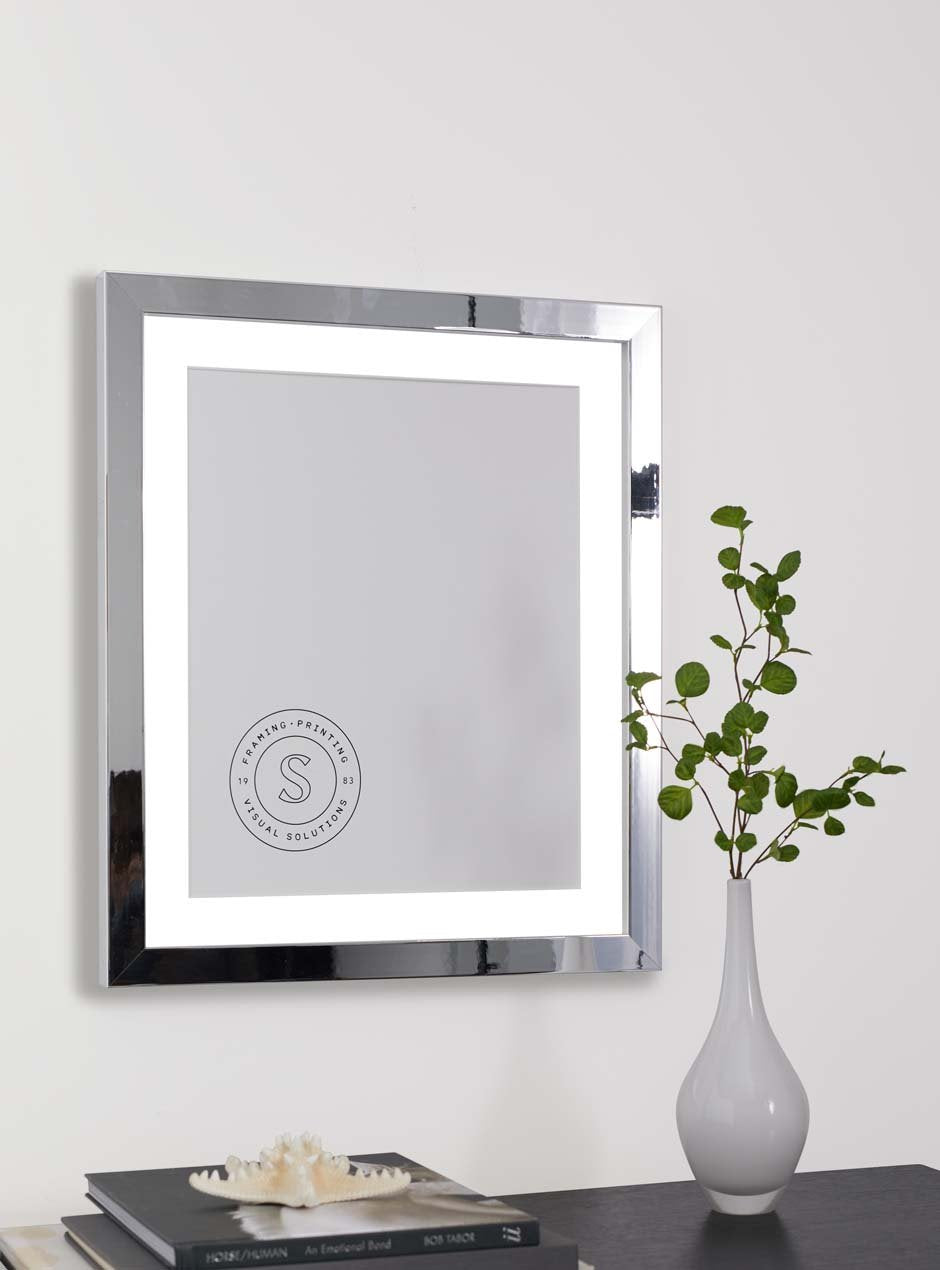 mirrored frame with skyframe logo inside hung above a table with plant in a vase and a book stack with a starfish on top