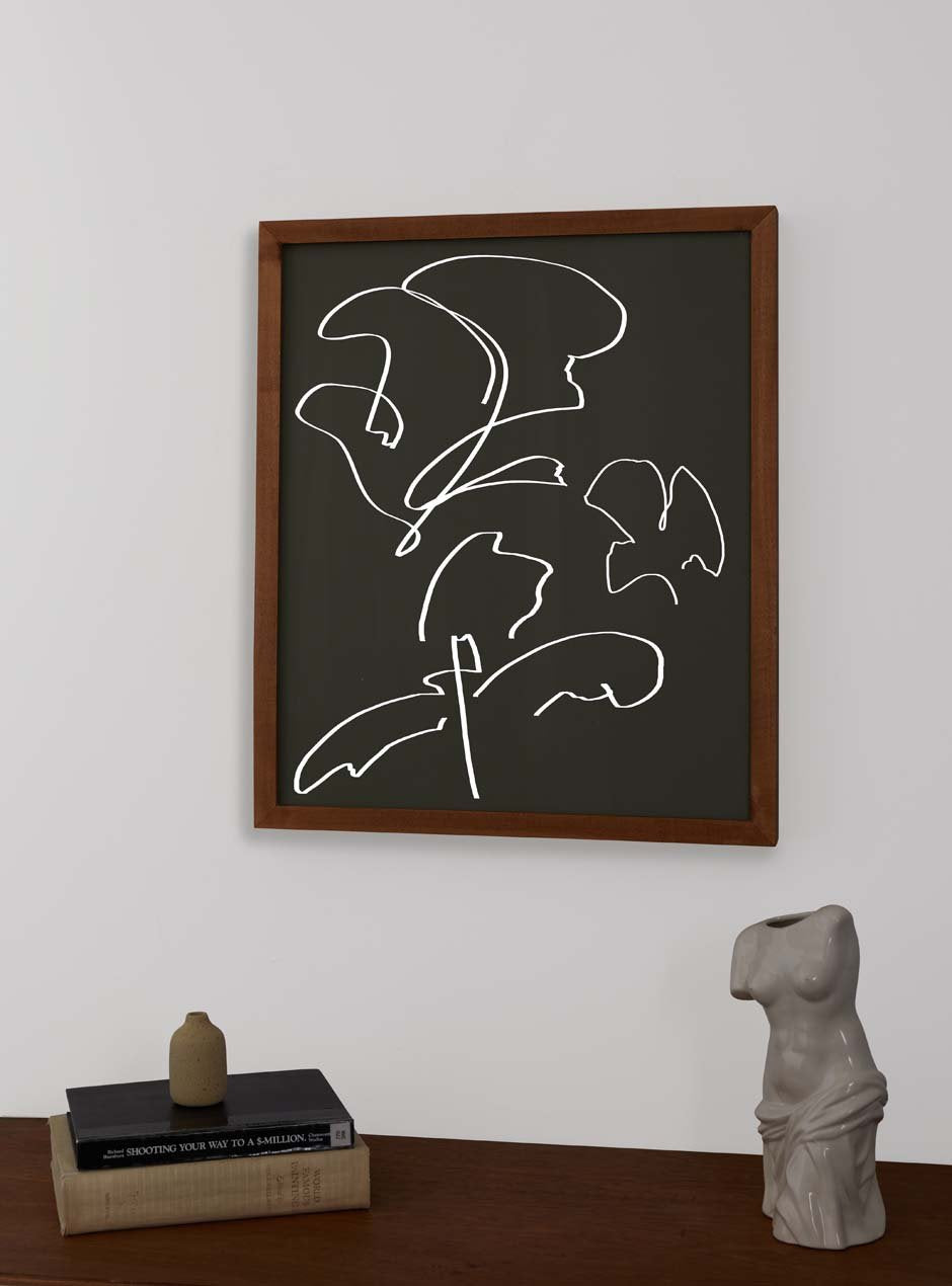 maple frame holding abstract art hung above table with various objects 