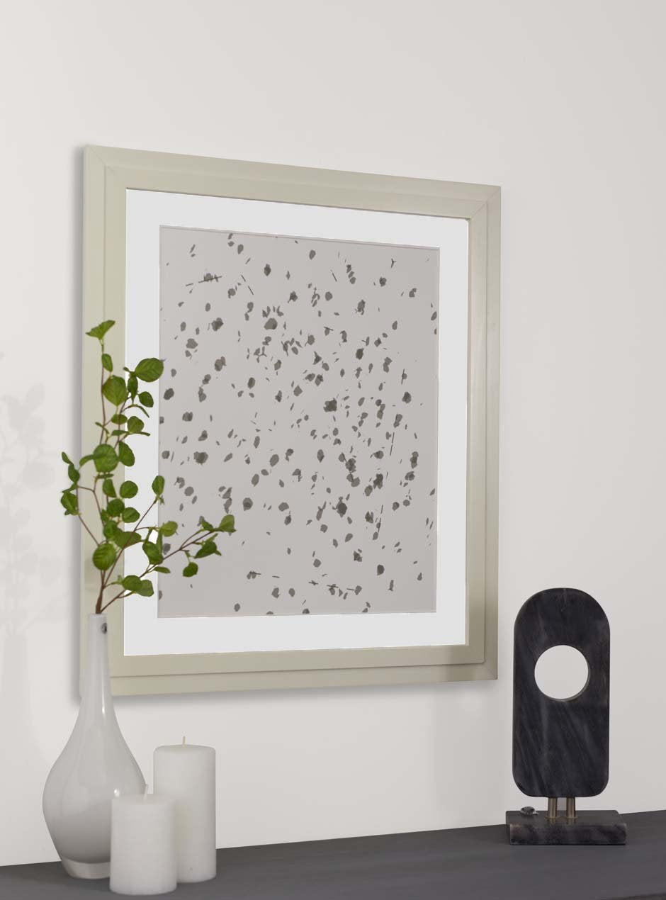 grey abstract on white background in light wood frame with white matting hung above a table with  candles and a vase with branches