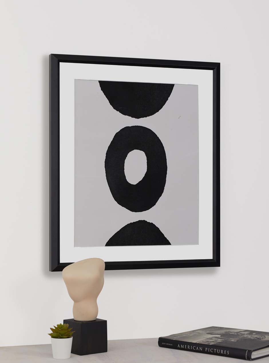abstract circle on white background with black frame and white matting hung above a table with sculpture, succulent and book