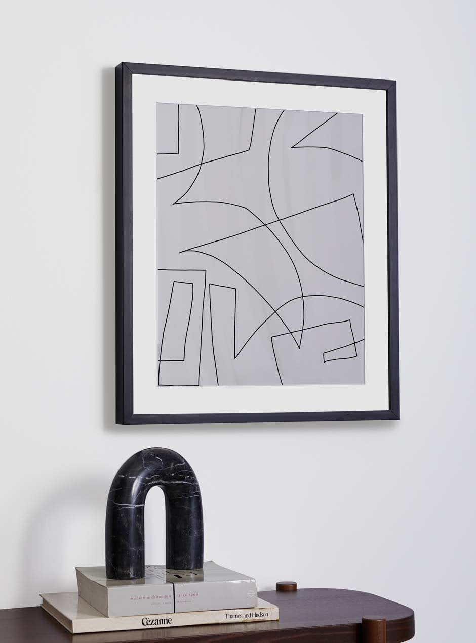 thin modern black wood frame with white matboard and linear modern abstract artwork on a white wall with a dark wash wooden table in front with modern abstract decor and two books