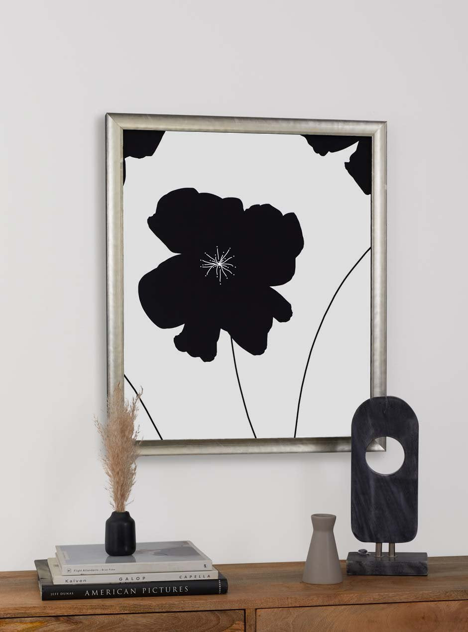 silver frame holding abstract flower art hung above table with various objects