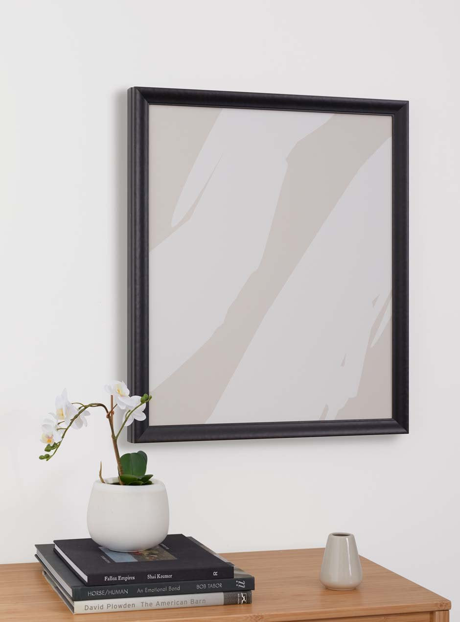 black textured picture frame with pitched down moulding style with abstract neutral artwork and table below with small orchid in white vase and several art books