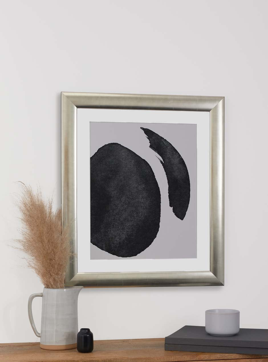 silver frame holding abstract black and white painting hung above table with various small objects